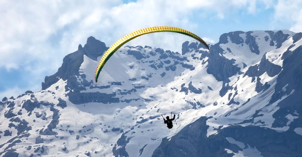 Un parapentiste plane au-dessus de majestueux sommets enneigés, capturant l'esprit d'aventure.