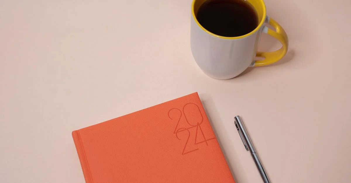 Mise en scène élégante d'un planner 2024 avec du café et un stylo sur un fond pêche.