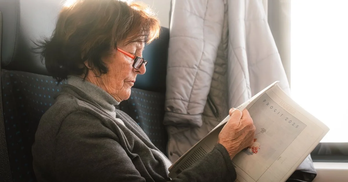 Une femme âgée lisant un journal pendant un voyage en train, capturant un moment serein.