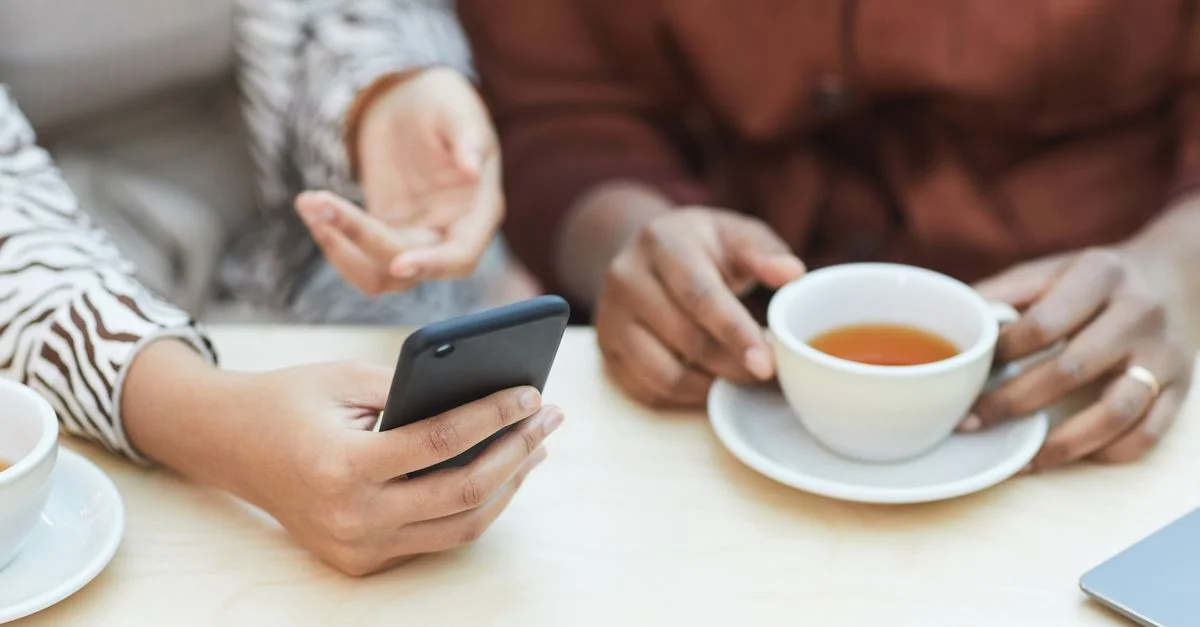 Deux collègues partageant des idées, avec un smartphone et un café, dans un cadre collaboratif.