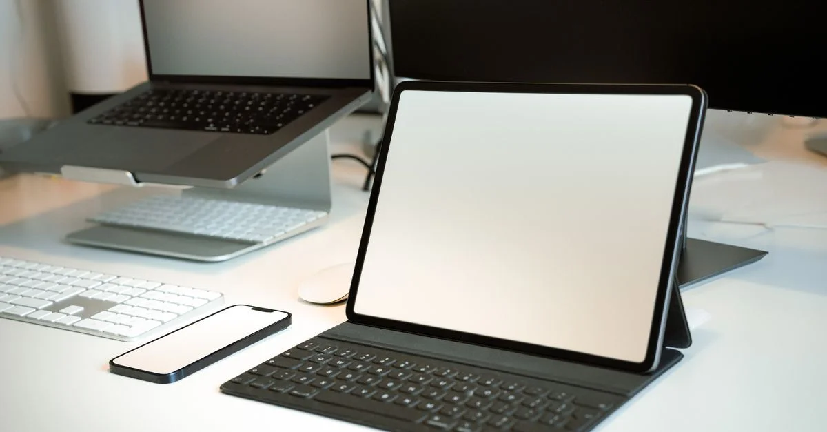 Un espace de travail propre et moderne avec un ordinateur portable, une tablette, un smartphone et des accessoires sur un bureau.