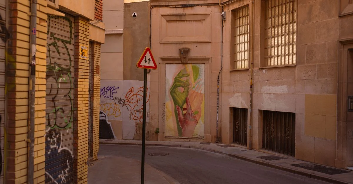 Des œuvres de street art colorées représentant des mains décorent une ruelle urbaine mêlant graffitis et architecture sobre.