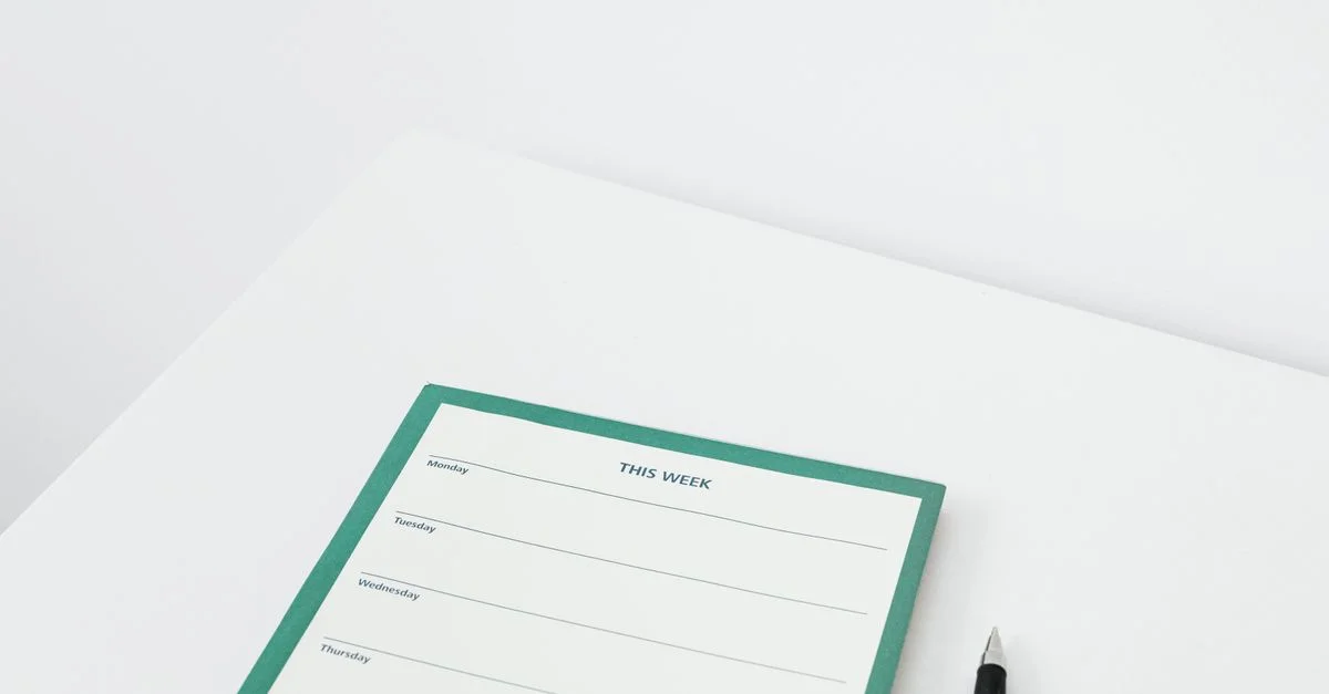 Un planificateur hebdomadaire propre et minimaliste avec un stylo sur un bureau blanc, parfait pour organiser efficacement votre emploi du temps.