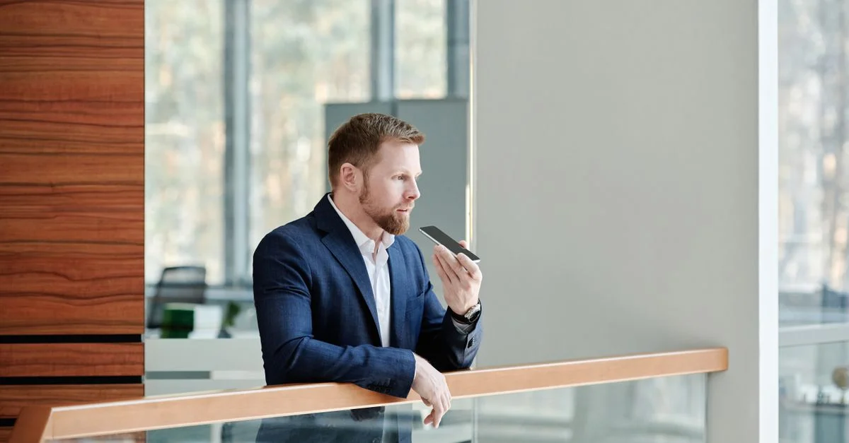 Homme d'affaires professionnel tenant un smartphone et parlant à l'intérieur d'un bureau moderne.