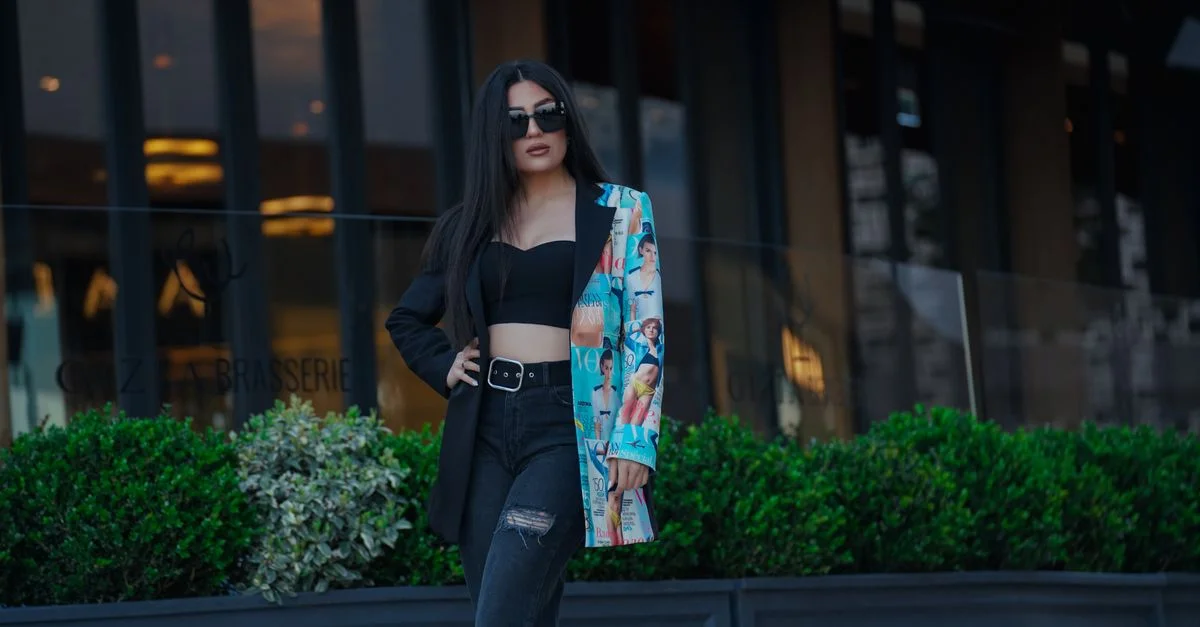 Portrait de mode chic d'une femme portant des lunettes de soleil et une veste colorée dans la ville.