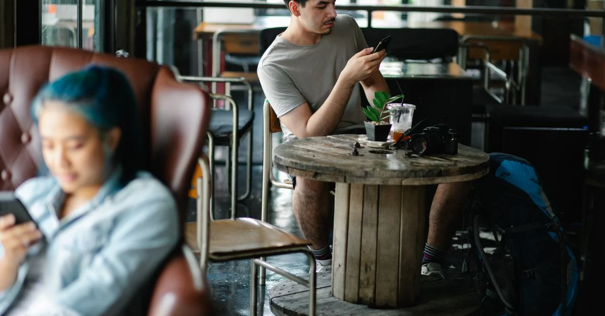 Jeunes adultes utilisant des smartphones dans un café chaleureux, capturant le style de vie moderne et la connectivité à l'intérieur.