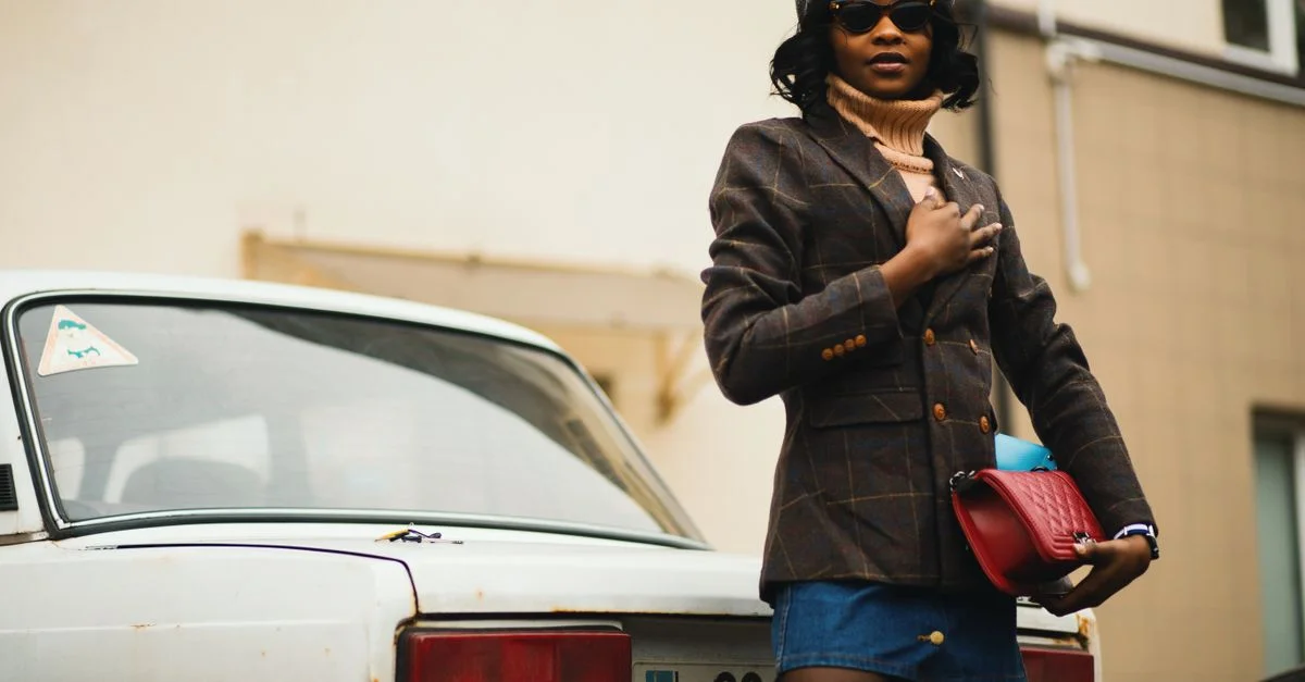Une femme élégante en tenue à la mode pose avec confiance près d'une voiture classique en plein air. Parfait pour des thèmes de mode et de style de vie.